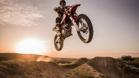 Low angle view of Enduro motocross rider jumping high up off-road at sunset. Copy space.